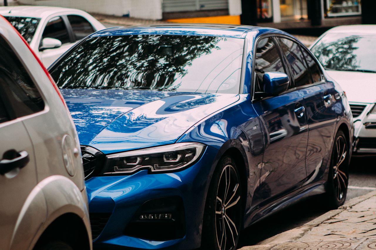 A vibrant blue luxury sedan parked on an urban street among cars.